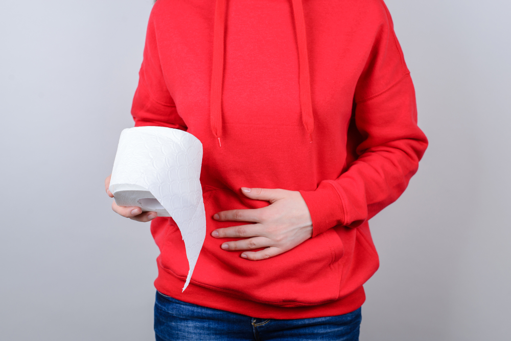 Unhappy woman holding her gut with one hand and a roll of toilet paper in another