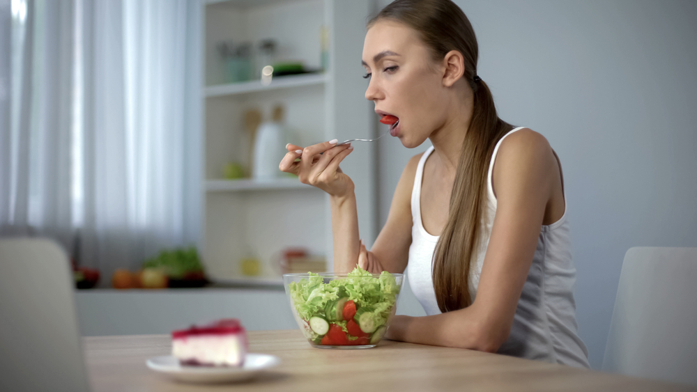 woman eating salad while looking at a slice of pie